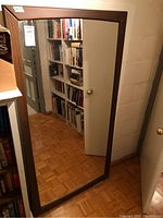 Front view of the wall mirror reflecting a bookshelf and door, showing the rectangular shape and wooden frame.