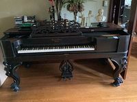 Front left angle view of the piano showing the carved rococo legs, music rack, and keybed with some wear.