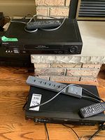 Full view of the Sony VHS player on the fireplace ledge and the Panasonic DVD/CD player on the floor with power bar and remotes visible.