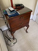 Front and top view of vintage wooden side table with scuffs and scratches, glass top with beveled edges, and decorative brass handles on drawers. Shows the overall condition and design details.