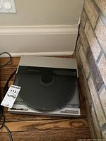 Technics Quartz direct drive turntable model SL-7 shown from above with dust cover closed, placed on wooden floor next to wall and fireplace corner. Has wear and vintage look.