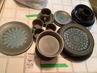 Overview of the collection showing plates, bowls, and cups stacked on a kitchen counter.