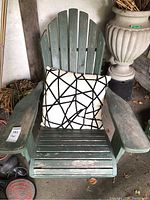 Front view of weathered green wooden Adirondack chair with beige and black patterned pillow on seat, showing paint wear and slatted design.