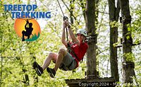Person zip lining through forest trees wearing a helmet and harness, representing part of the Treetop Trekking experience.