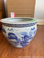 Front view of the large blue and white ceramic plant pot showing detailed landscape painting and geometric border on rim.