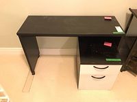 Full view of desk with filing cabinet under right side, showing black surface with visible wear.