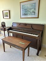Full view of Ennis upright piano with matching wooden bench placed in front and part of the room background visible