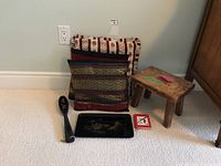 Wide shot showing all items: two decorative pillows, wooden foot stool, black lacquer serving spoon and tray, Feng Shui book, arranged on floor.