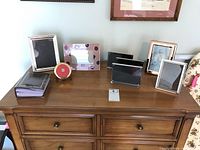 View of eight various picture frames and one small photo album displayed on a wooden dresser.