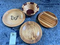 Set of four handcrafted wood pieces: butterfly plate, segmented bowl, striped plate, natural grain plate.