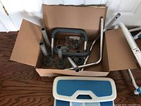 Parts of the shower chair laid out including metal frame sections, armrests, legs, and a padded seat with blue top.