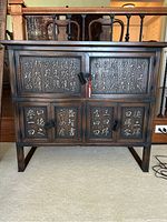 Front view of vintage Korean chest showing three sets of cupboard doors with carved calligraphy inscriptions and a red tassel hanging from metal ring handle.