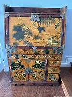 Front view of Korean secretary desk showing detailed hand-painted panels with birds, flowers, and nature motifs. Brass hardware and corner accents visible. Hinged drop front closed.