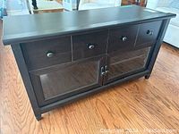 Front angled view of the modern wooden TV stand showing four top drawers and two glass-door cabinets below with shelving inside.