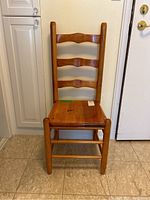 Front view of the pine ladder back chair showing three horizontal ladder slats and solid wood seat with scratches.