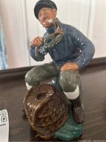 Front left angle of the Royal Doulton lobster man figure showing seated fisherman, lobster and lobster pot detail