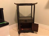 Front view of small Asian themed occasional display stand showing two drawers and cupboard with open doors.