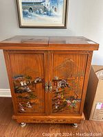 Front view of vintage wooden bar cabinet with detailed Asian themed painted scenes on the two front hinged doors.