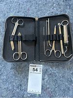 Opened leather case showing vintage minor surgery tools arranged in elastic bands including scissors, forceps, and other metal instruments with visible wear on the case.
