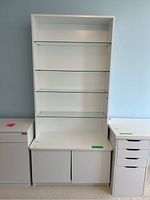 Full view of the white bookcase with four glass shelves and lower cabinet showing two doors.