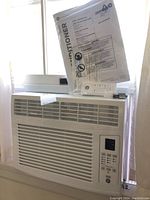 Front view of GE window air conditioner in window, showing vents and manual in plastic atop the unit.