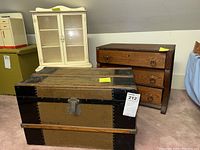 Wide shot showing the antique storage trunk, painted hutch and wooden dresser grouped together on carpeted floor.