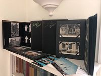 Photo showing multiple vintage postcard albums open on a shelf, some postcards displayed inside and others laid in front.