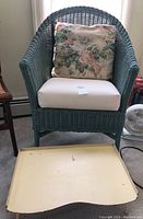 Wicker chair with cushion and floral pillow alongside a yellow lap desk placed on the floor.