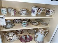 Shelf with assorted teacups, mugs, saucers, two teapots, and cream and sugar set.