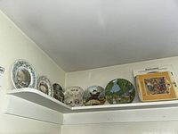 Collector's plates arranged on a shelf showing multiple decorative plates including a boxed Villeroy & Boch Kinderspiele plate.
