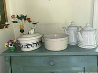Overall view of the lot showing floral metal candelabra, ceramic dishes including Dedham pottery crock, Pfaltzgraff baking dish, and Winterling tea and coffee pots.