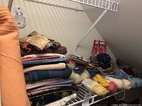 Wide view of shelf with folded fabric pieces, bundle of yarns, and knitting supplies