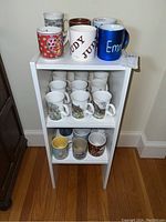Full set of assorted mugs displayed on a three-tier white shelf