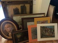 Display of multiple framed prints including an oval portrait of George Washington and various landscape prints and paintings with different frame styles and mats.