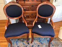 Pair of antique solid wood framed chairs showing full front view with black fabric upholstery and carved wood details on backrests.