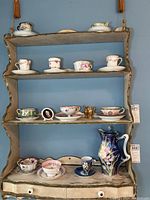 Wide shot of shelf displaying various teacups, saucers, miniature jugs, small framed portrait, and cobalt blue teapot.