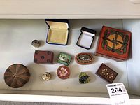 Top-down view of assorted small jewelry and trinket boxes arranged in a drawer, showing various materials and styles including wooden, metal, woven, and velvet-lined boxes.