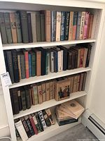 Wide view of white bookshelf holding 4 shelves of assorted vintage and antique hardcover books arranged upright