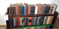 Two wooden shelves with approximately 40 vintage and antique books including various hardbound literature with worn spines and covers.