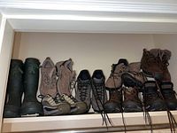 Six pairs of women's hiking and rain boots in various colors and styles including green rubber rain boots, and tan and brown hiking boots.