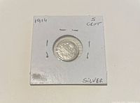 Photograph of the 1914 Canadian 5 cents silver coin inside a white cardboard holder with handwritten labels and staples around the edges.