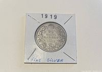 Reverse side of 1919 Canada 50 cents silver coin showing denomination surrounded by maple leaves in white protective holder with '1919' and 'Fine Silver' markings.