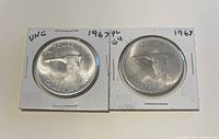 Two 1967 Canadian silver dollar coins in protective holders showing the hummingbird side, with inscriptions of denomination and year.
