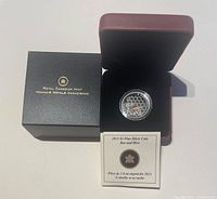 Photo showing the 2013 Canada $3 fine silver coin featuring a bee and hive design in a capsule, inside a red velvet-lined presentation box, with the certificate of authenticity booklet.