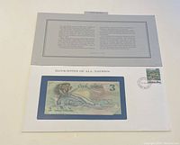 Front side of the Cook Islands 3 dollar banknote visible through a protective holder in a white envelope with a printed descriptive card and an affixed postage stamp with postmark.