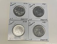 Front side of four French 5 Francs coins from 1970, 1972, 1978, and 1987 capped in white holders indicating year and denomination.