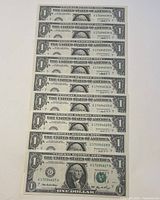 Nine sequential 2006 US one dollar bills arranged in a fan shape showing the front side with clear serial numbers.