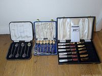 Full view of the three cases containing spoons and knives laid out on floor showing contents.