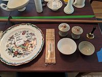Tabletop view showing decorative plate, disposable chopsticks, ceramic spice jars, small bowls, bamboo rod, and small brass bell