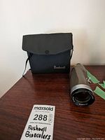 Bushnell binoculars with carrying case shown side by side on a wooden surface